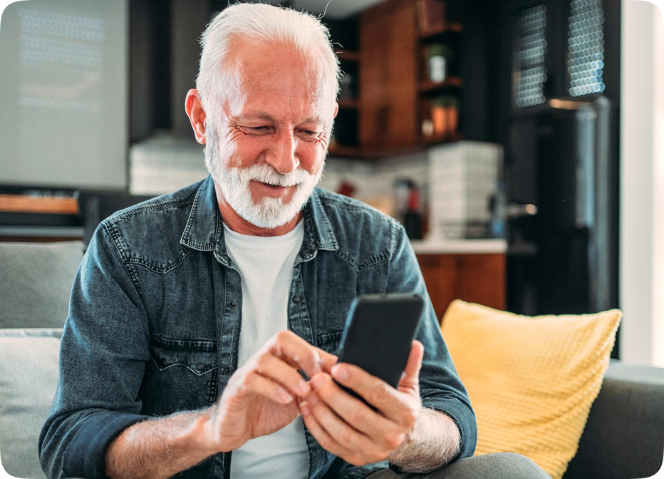 Smiling older man using smartphone comfortably at home, demonstrating easy control of Audien hearing aids via app