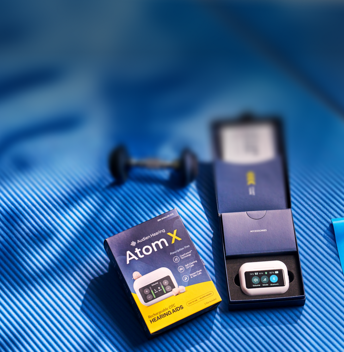 Atom X hearing aids packaging on a blue mat with dumbbells in the background